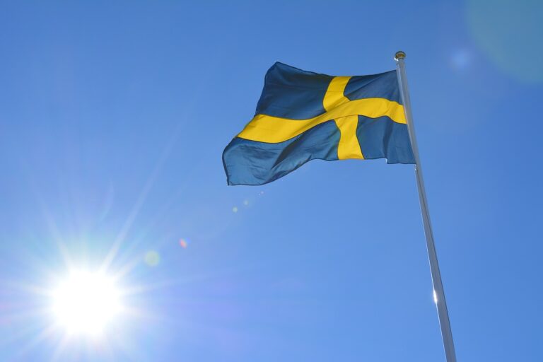 Swedish flag waving against a clear blue sky and sun flare in Stockholm