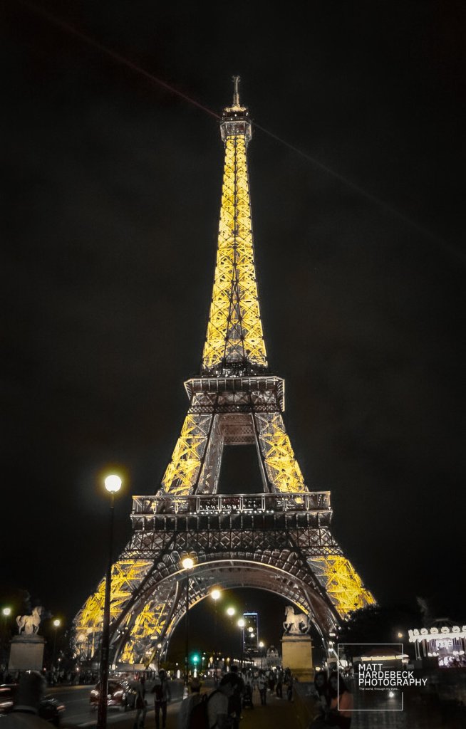 The Eiffel Tower illuminated in gold, glowing above the nighttime crowds on a lively Paris evening.