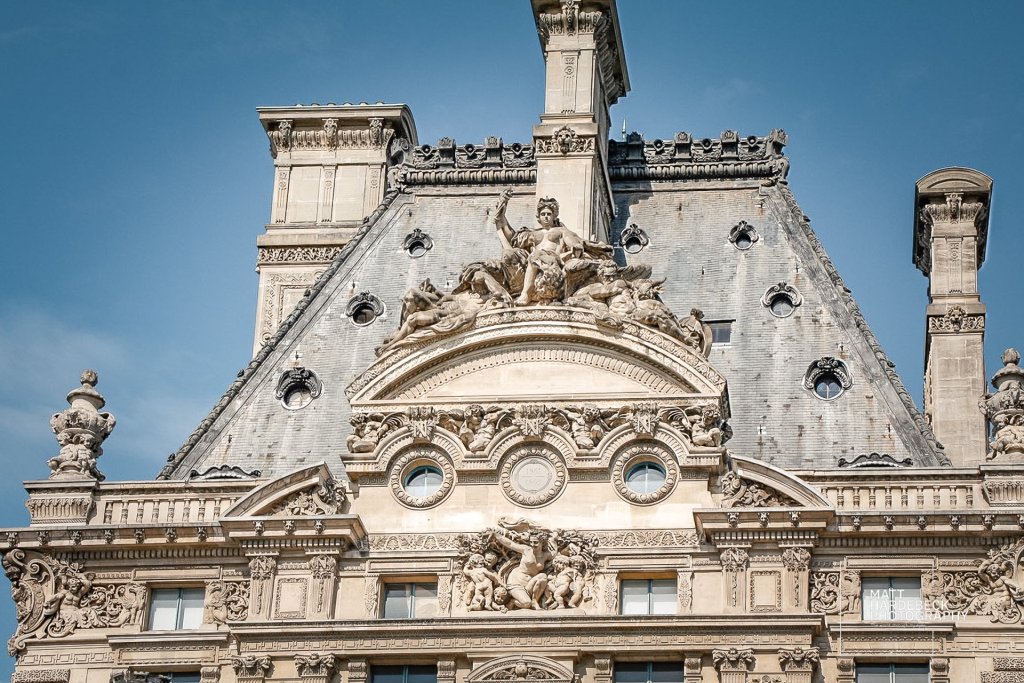 Classical statuary crowning the sloped slate roof of the Louvre.