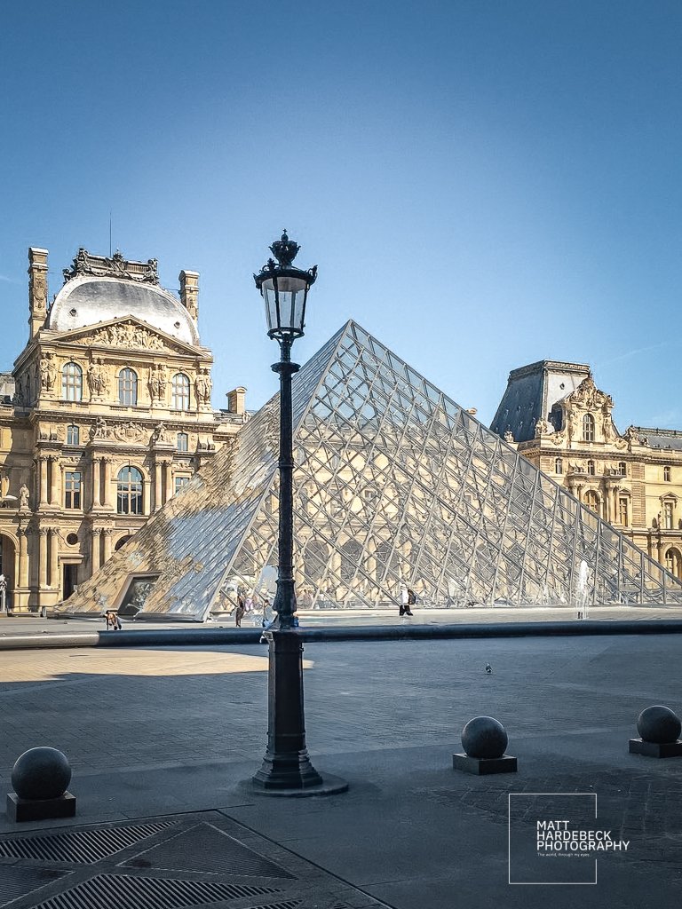 Wide view of the glass pyramid framed by historic palace wings.