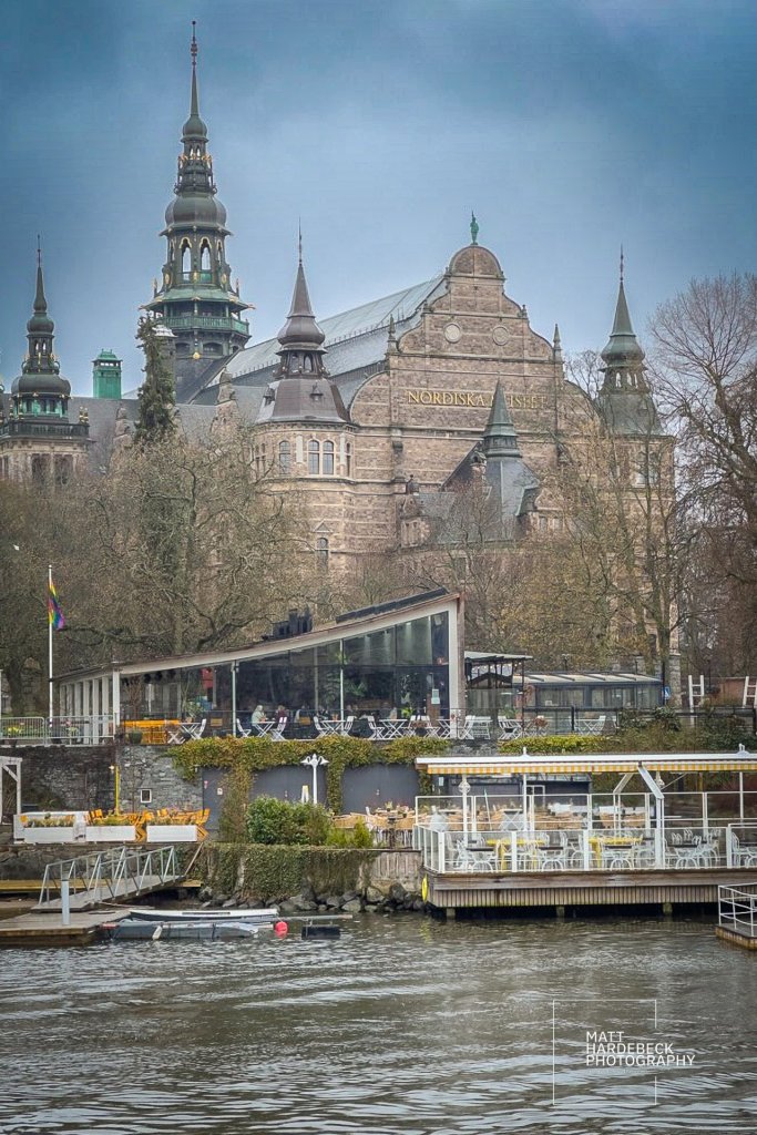 Exterior view of the Nordiska Museet with dramatic spires rising behind waterfront cafés.