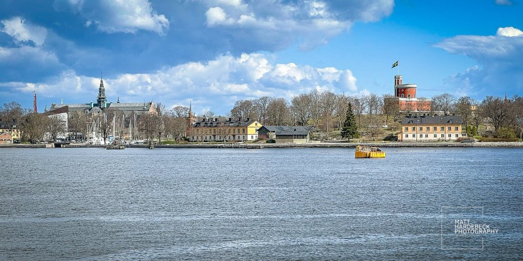 View of Djurgården across the bay, showcasing the Nordiska Museet and Kastellet tower under blue skies.