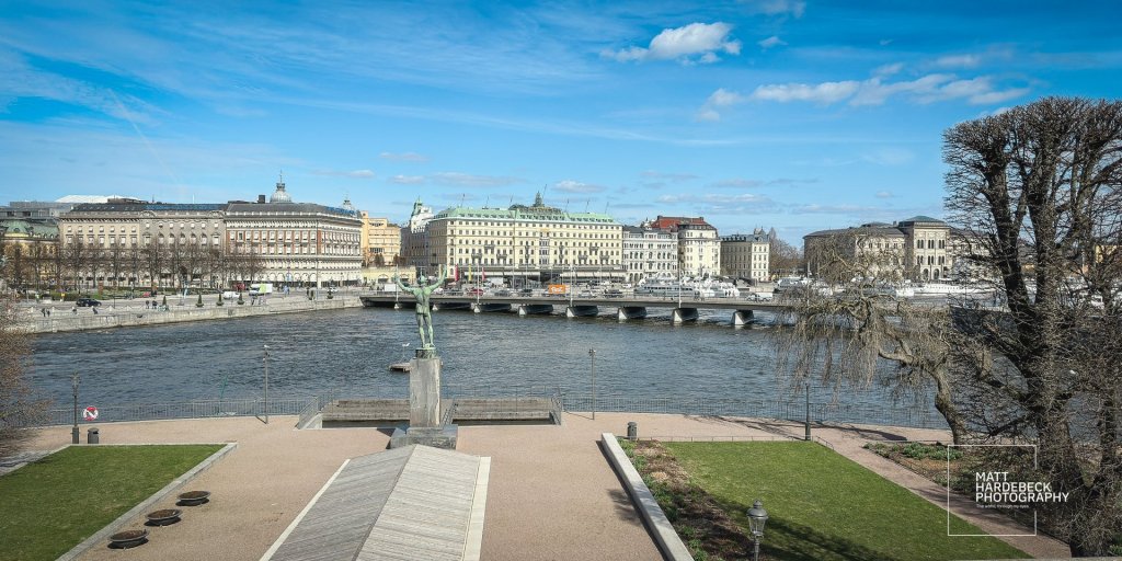 Statue and city skyline seen from the terrace behind the Royal Palace, with the bridge and Riksdag in view.