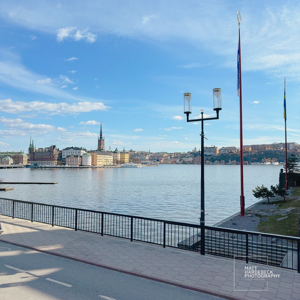 Stockholm skyline across Riddarfjärden, framed by lampposts and flags.