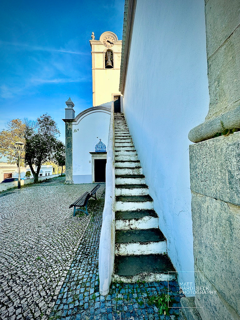 Narrow outdoor staircase leading to the bell tower of a whitewashed church in Almancil, Portugal.