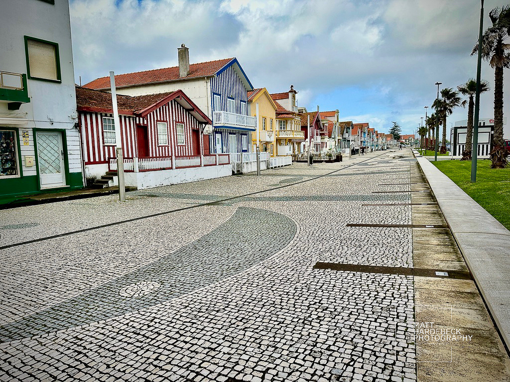 Striped houses along a cobblestone promenade in Costa Nova, Aveiro, Portugal.