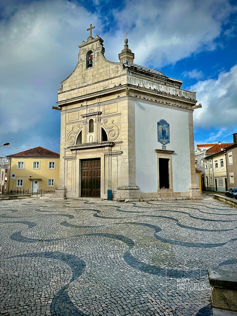 Historic stone church with azulejo tile detail in Aveiro, Portugal, framed by a patterned cobblestone square.