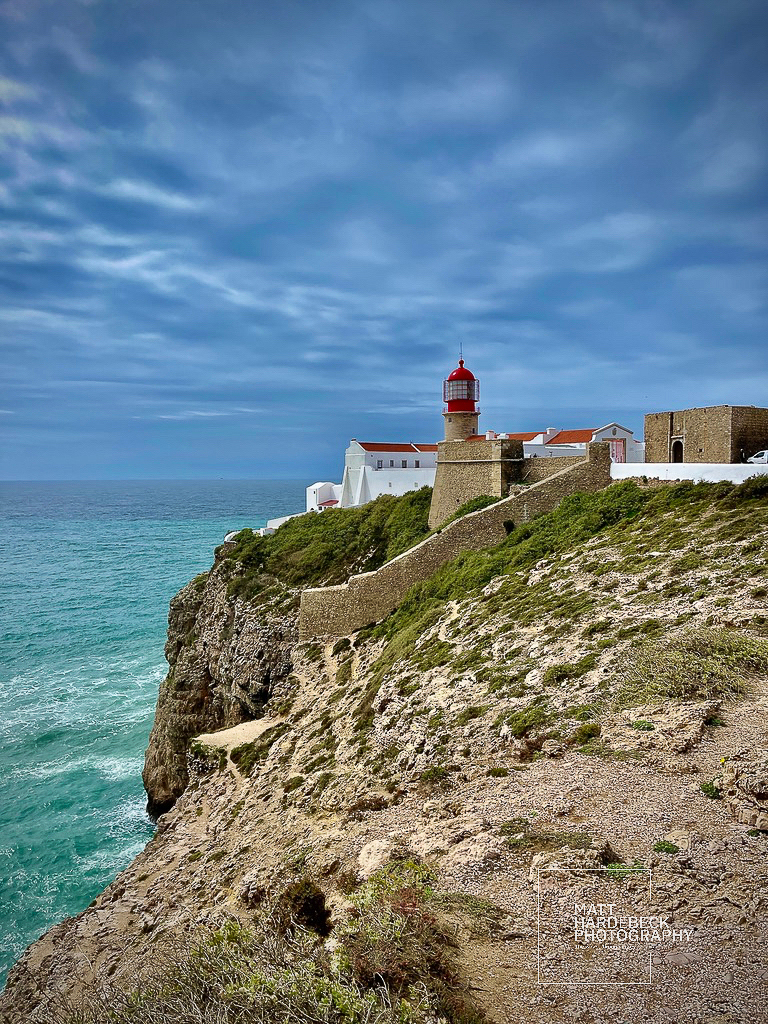 Red and white lighthouse perched on cliffs above the Atlantic Ocean at Cabo de São Vicente, Portugal.