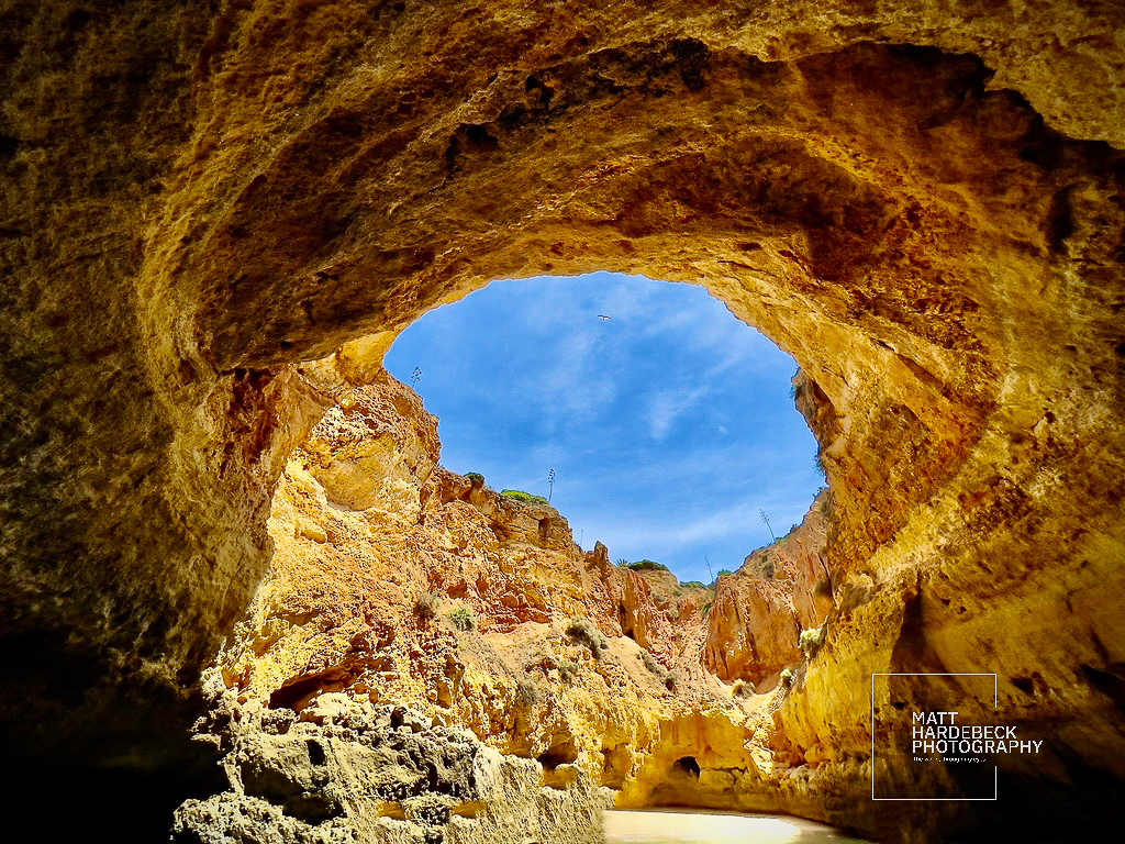 iew from inside a sea cave looking out toward blue sky and rock formations in the Algarve, Portugal.