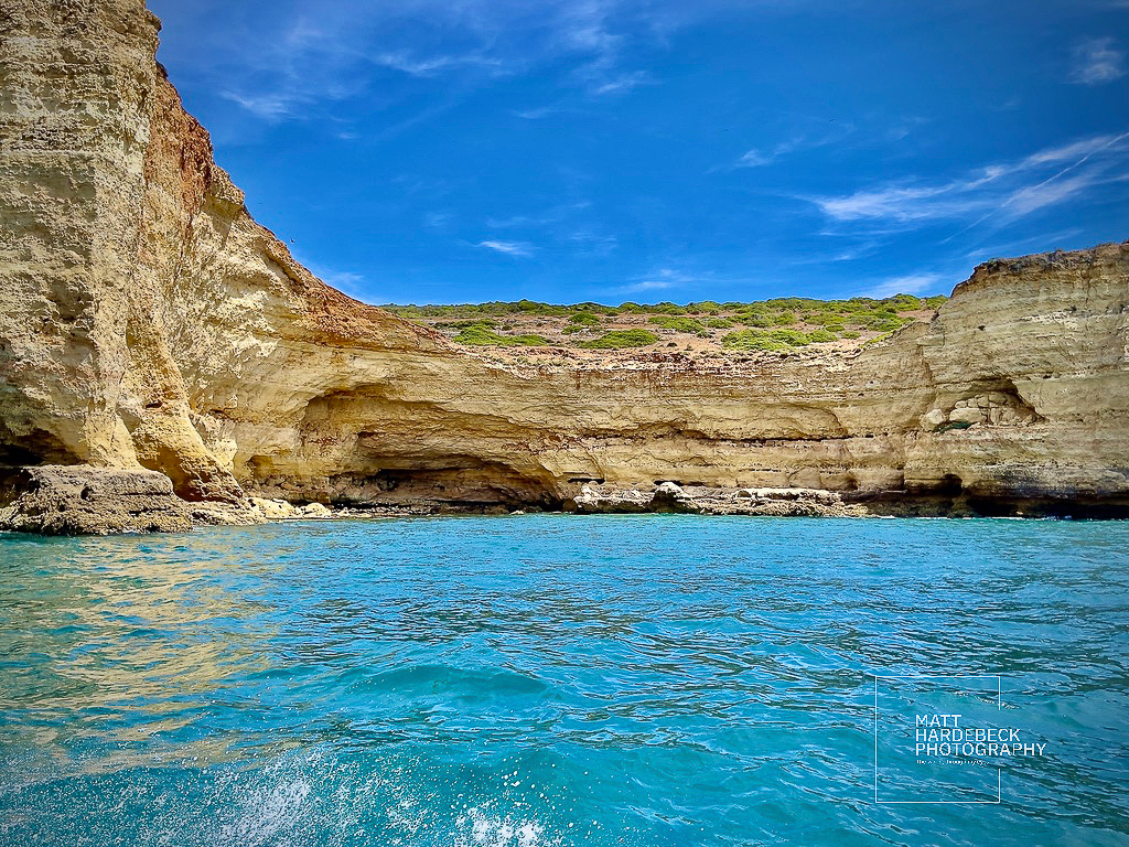 Sheer limestone cliffs meeting the turquoise waters of the Algarve coast under a vivid blue sky.