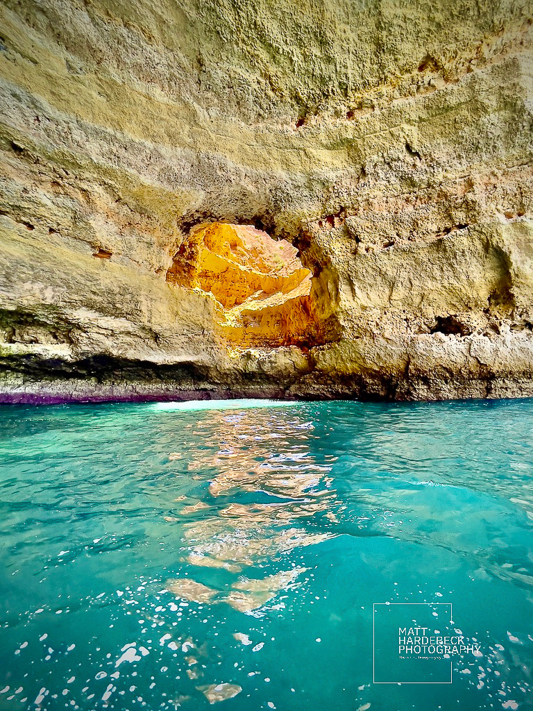 Sunlit rock opening inside a coastal cave reflecting warm tones onto the turquoise water.