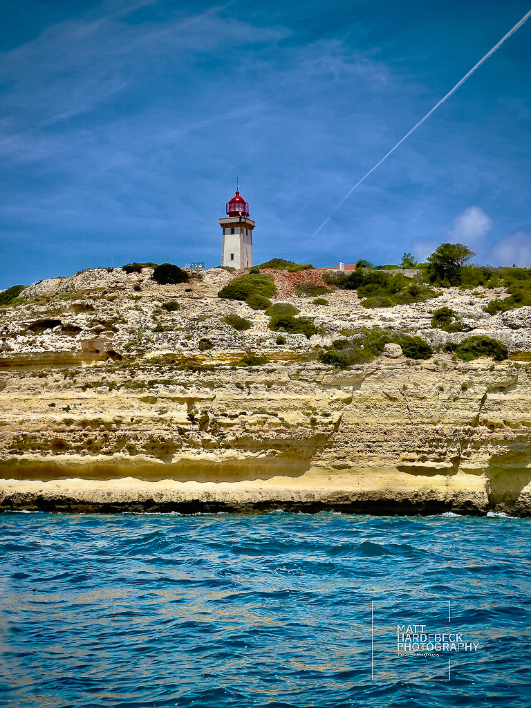 Red-capped lighthouse perched on layered limestone cliffs above the Atlantic Ocean.