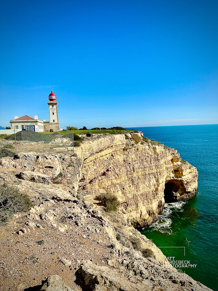 Lighthouse and keeper’s house atop sunlit cliffs overlooking deep blue waters.