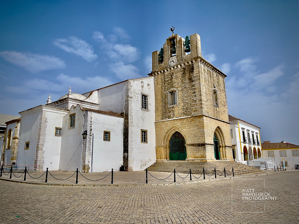 Historic whitewashed church with stone bell tower in Faro’s old town square.