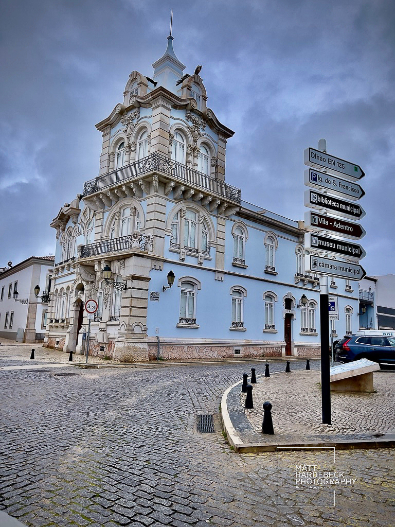 Ornate pastel blue corner building in Faro with decorative balconies and a tower against a cloudy sky.