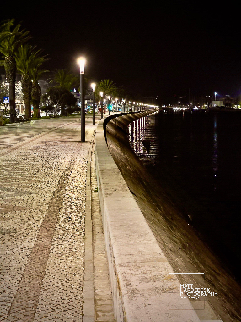 Illuminated promenade along the Lagos waterfront at night, with reflections in the water.