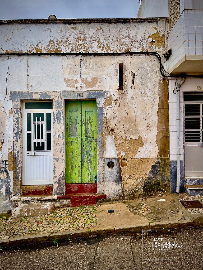 Weathered white house with a bright green wooden door in Fuseta.