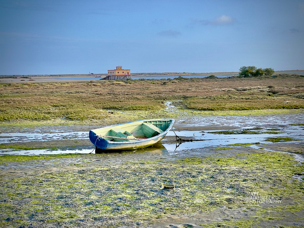 Single wooden fishing boat stranded at low tide in Fuseta, with the lifeboat station in the background.