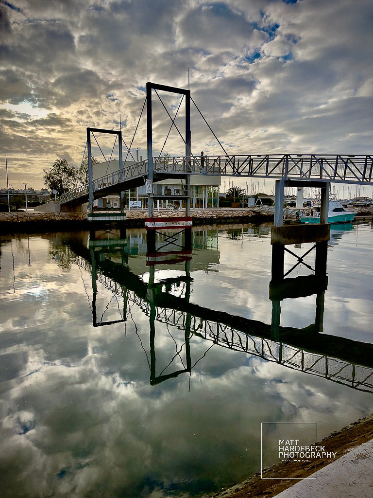 Pedestrian drawbridge to Lagos Marina, reflected in still water beneath a dramatic sky.