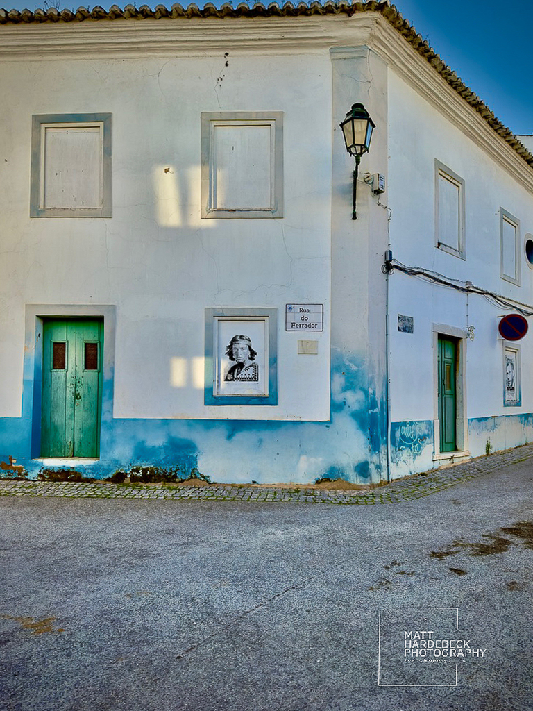 Whitewashed building in Lagos with teal doors, blue accents, and black-and-white portraits framed on the walls.