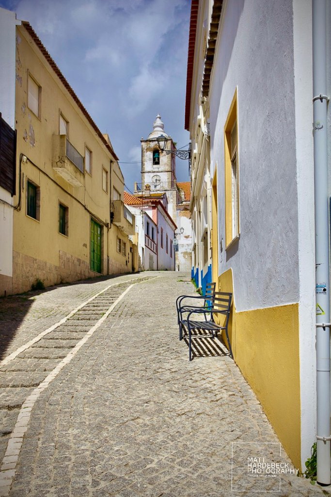 Steep cobblestone street leading to a church bell tower in Lagos, Portugal.