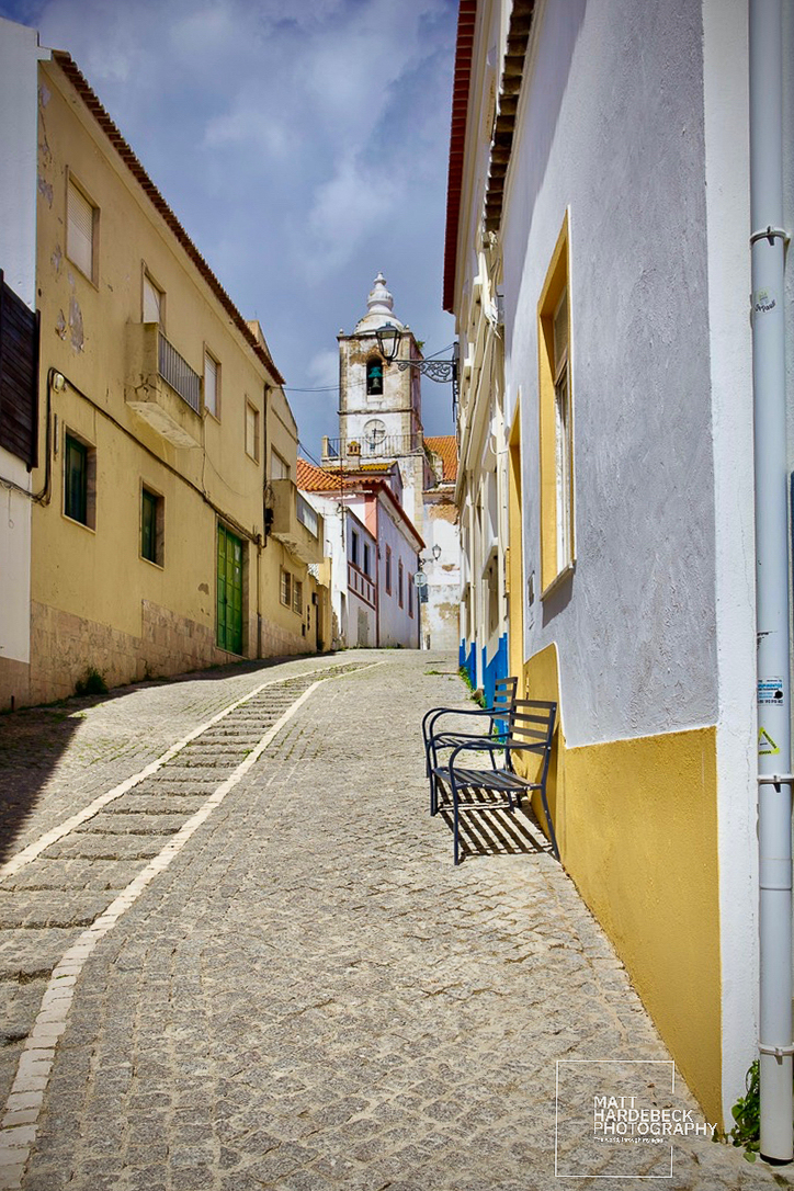 Steep cobblestone street leading to a church bell tower in Lagos, Portugal.