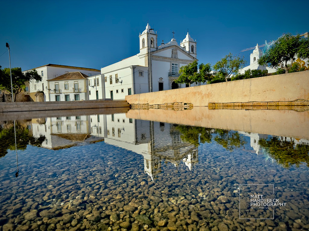 White church reflected in a shallow pool with stone bottom in Lagos, Portugal.