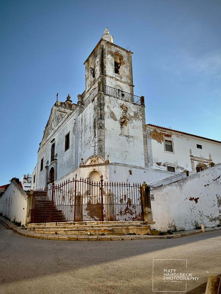 Weathered white church tower with red iron gate in Lagos, Portugal.