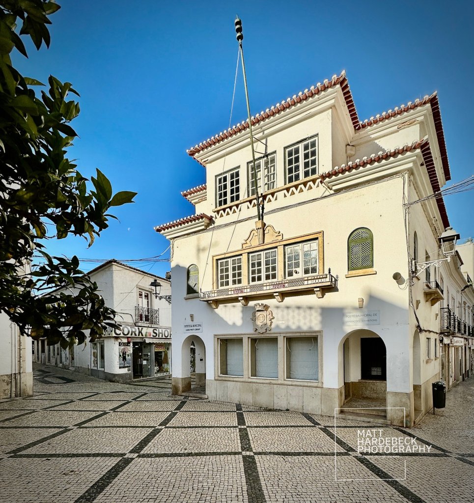 Historic whitewashed Post Office with tiled roof and patterned cobblestone square in Lagos, Portugal.