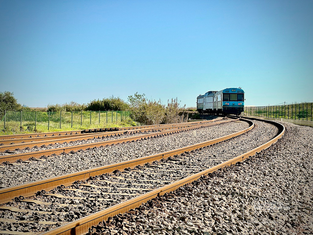 Blue and white train approaching on a curved railway track under a clear sky.