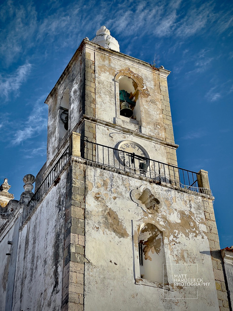 Weathered church bell tower with clock and peeling plaster in Lagos, Portugal.