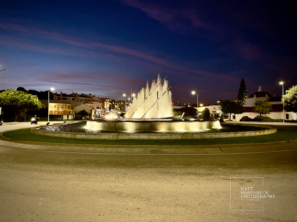 Illuminated roundabout fountain at dusk in Lagos, Portugal.