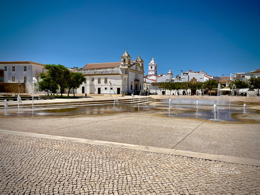 Public square in Lagos, Portugal, with fountains and the Igreja de Santa Maria in the background.