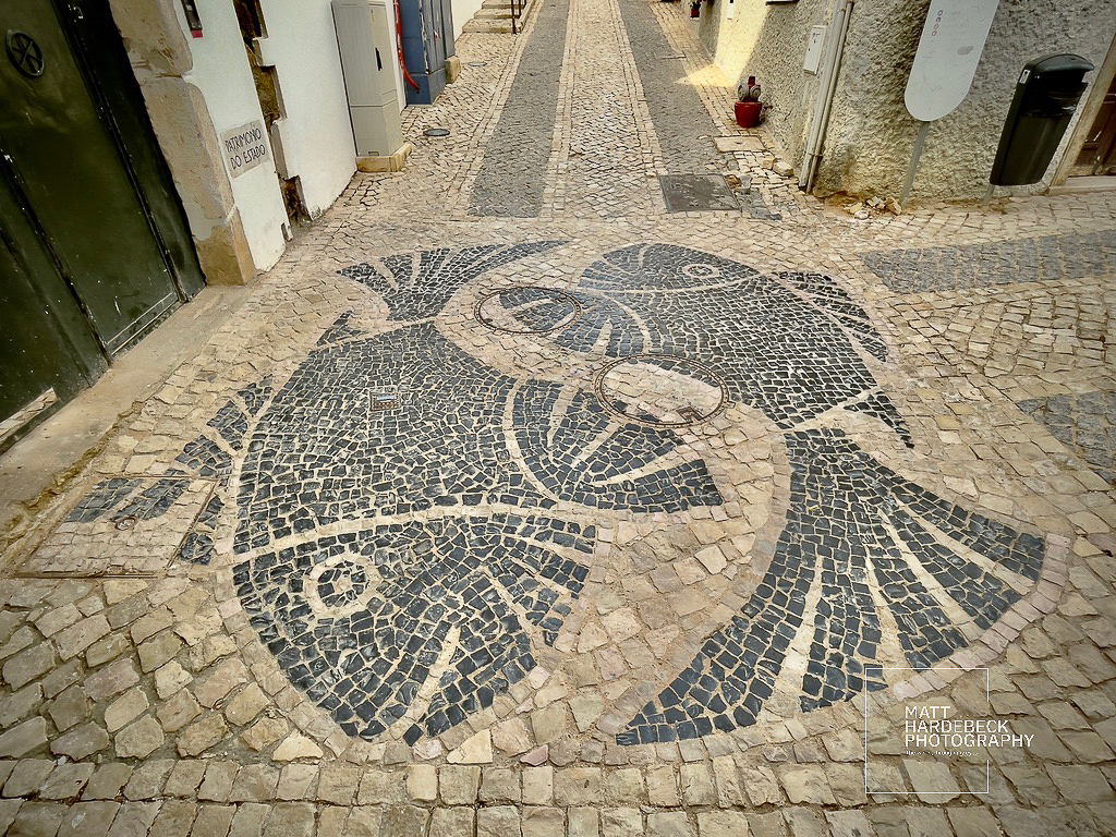 Mosaic of two fish in black and white stone on a cobblestone street in Lagos, Portugal.