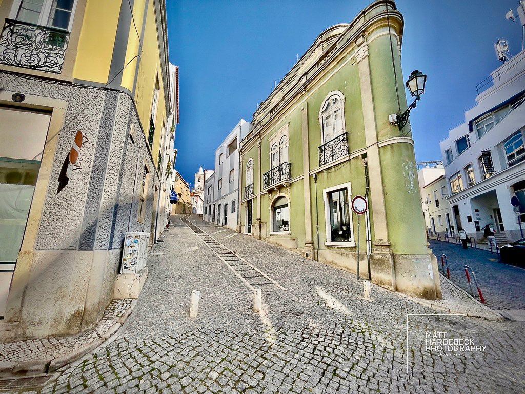 Narrow cobblestone street lined with colorful buildings in Lagos, Portugal, leading uphill.