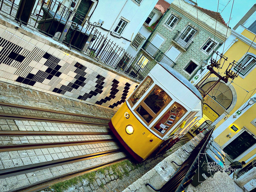 The Elevador da Glória funicular ascends a steep track past patterned tiles and traditional Lisbon architecture.