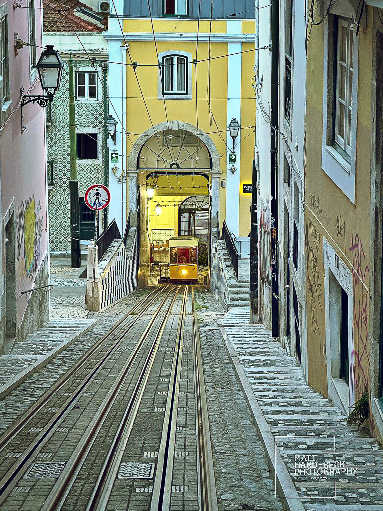 View down the steep track of the Elevador da Glória funicular framed by narrow buildings.