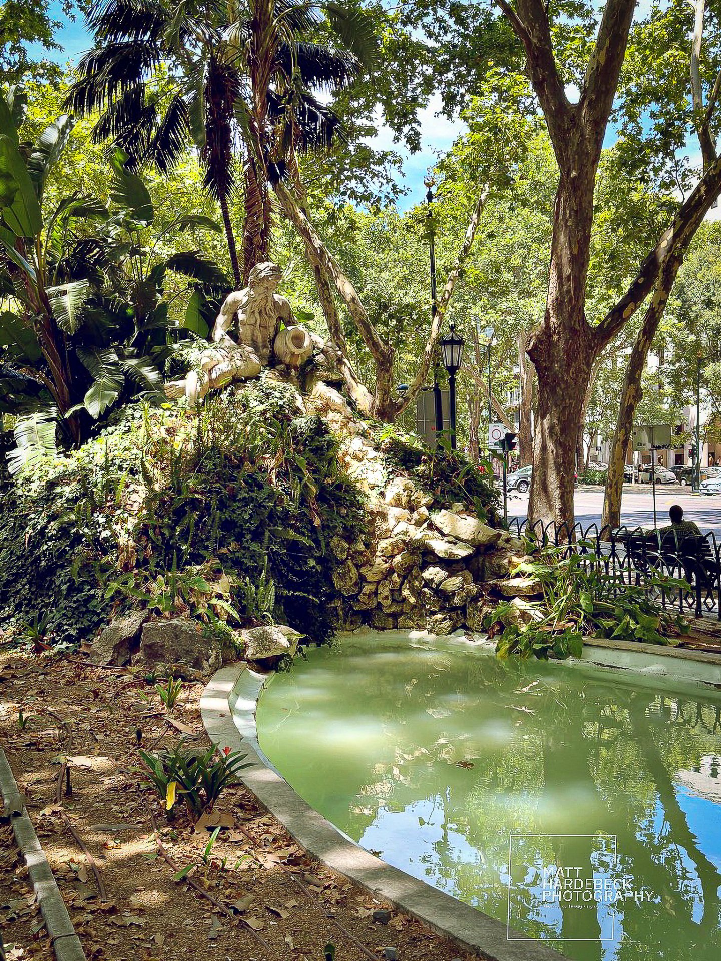A stone fountain and statue surrounded by lush greenery in a Lisbon park.