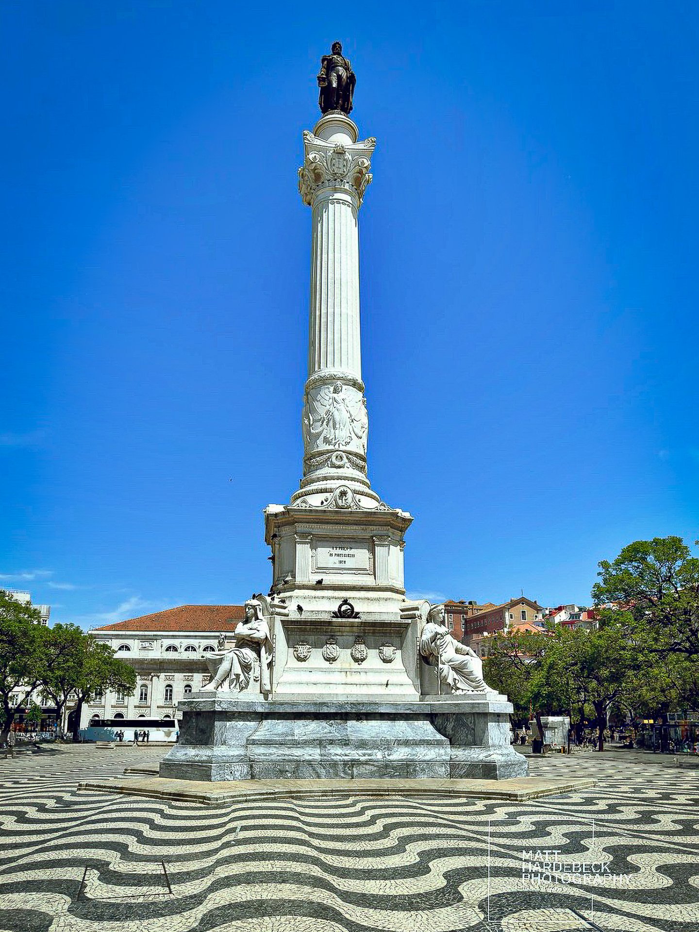 Statue of Dom Pedro IV atop a tall column in Rossio Square, Lisbon, with patterned pavement in the foreground.