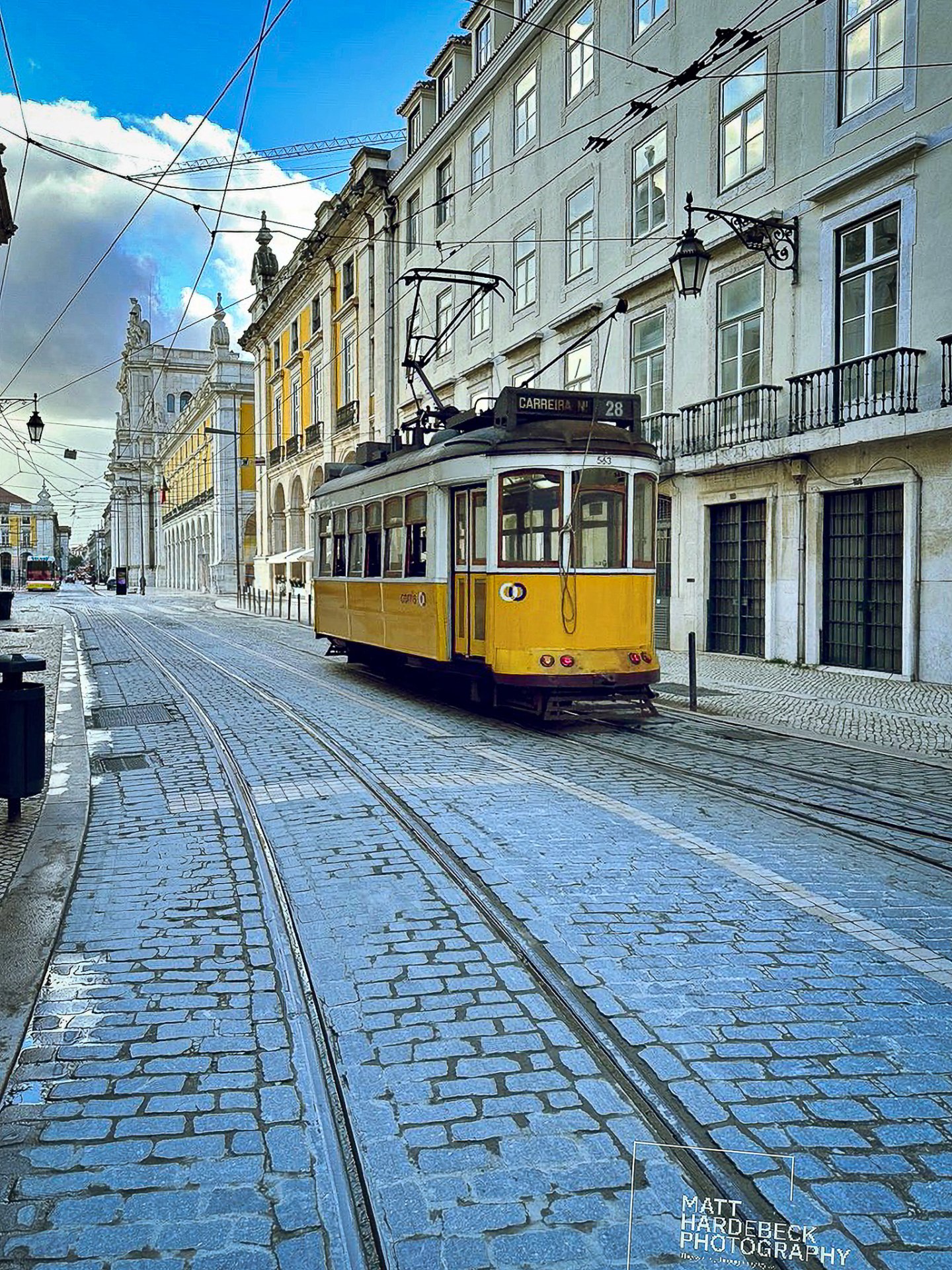Classic yellow tram on Route 28 traveling down a cobblestone street in Lisbon, Portugal.
