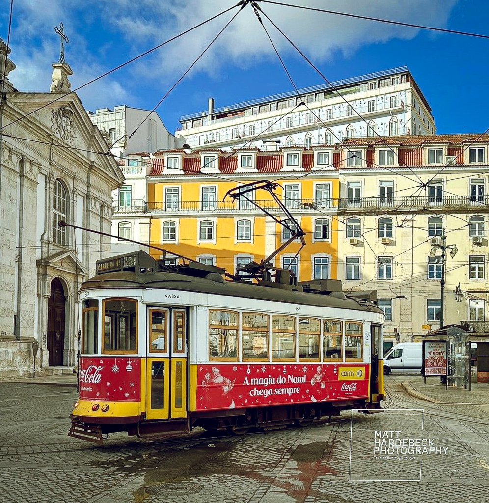 Lisbon tram decorated with Coca-Cola holiday branding passing by pastel-colored buildings.