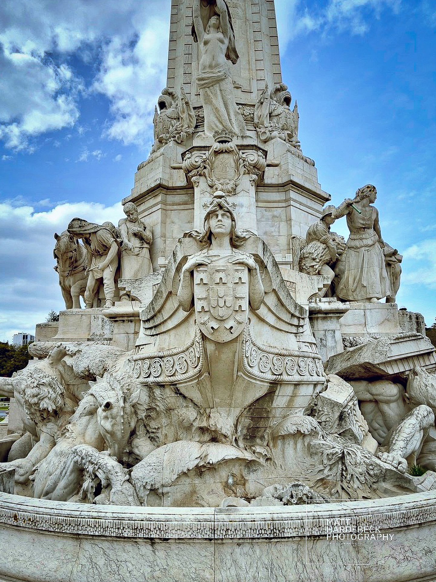 Close-up of the Monument to the Marquis of Pombal showing detailed sculptures of allegorical figures and a woman holding a shield.