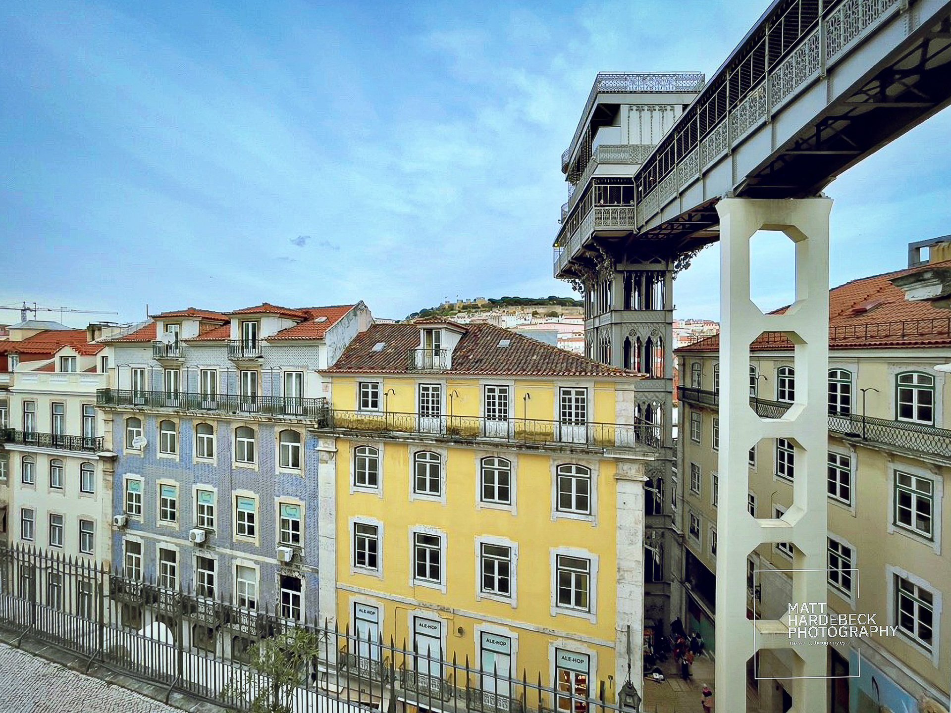 The ornate iron structure of the Santa Justa Lift connecting Lisbon’s Baixa district to Carmo Square, with colorful tiled buildings in the foreground.
