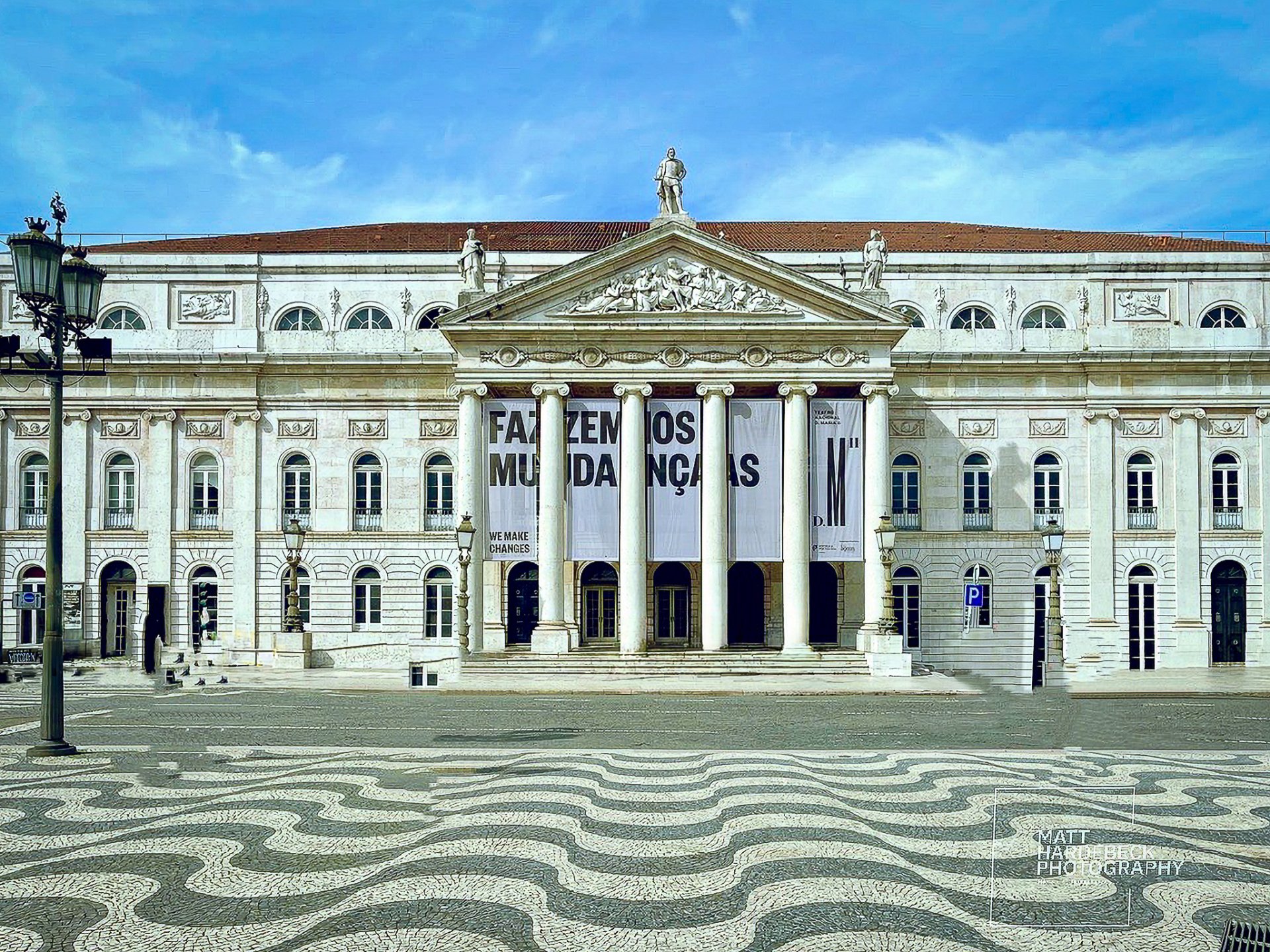 The neoclassical façade of Lisbon’s National Theatre D. Maria II with grand columns and a wave-patterned plaza in the foreground.