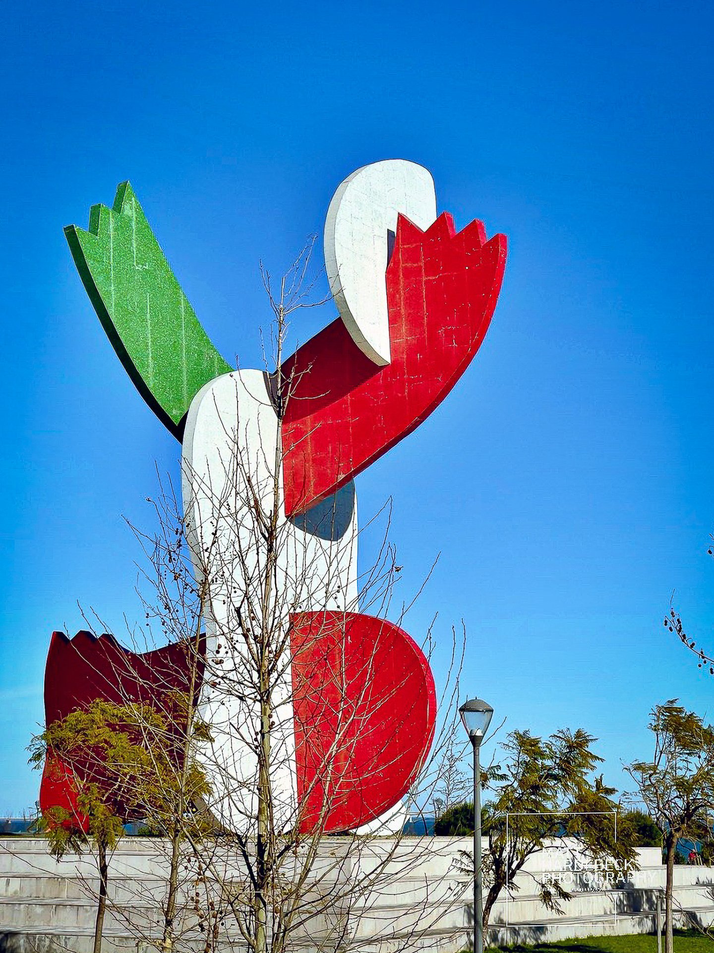Modern abstract sculpture in red, green, and white, representing Portugal’s national colors, set against a clear blue sky.