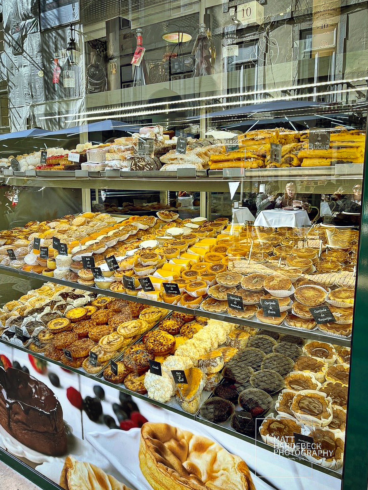 Display window of a Lisbon bakery filled with Portuguese pastries, including pastéis de nata, queijadas, and other sweets.