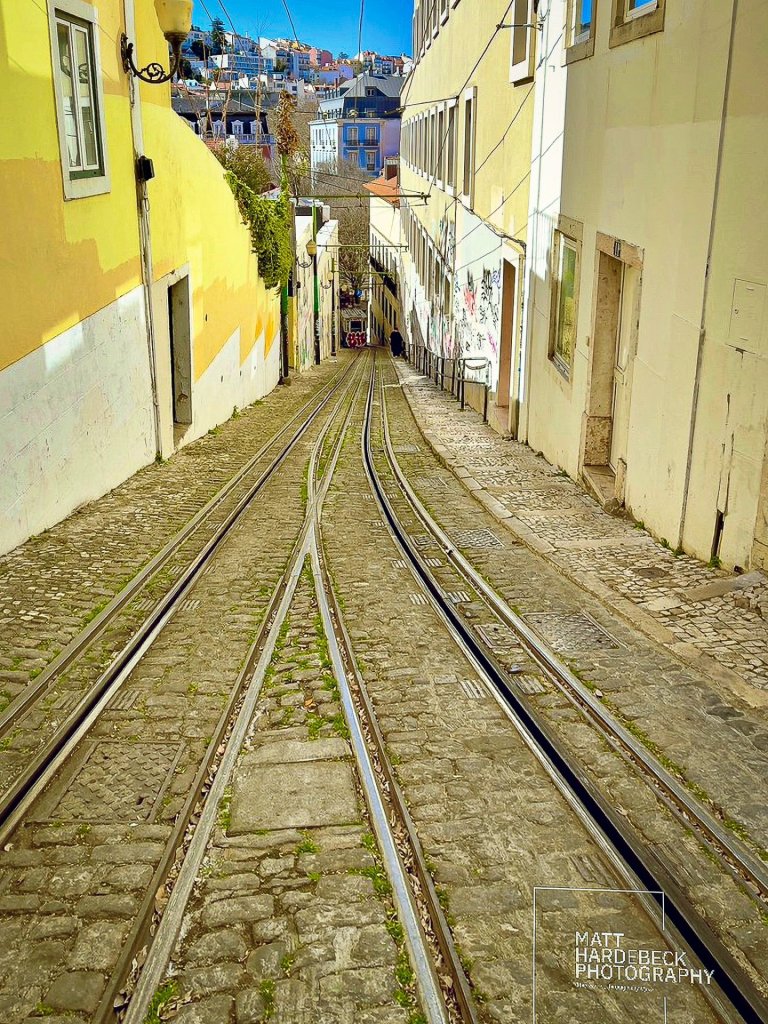 Steep cobblestone street in Lisbon with twin tram tracks running downhill toward the city.