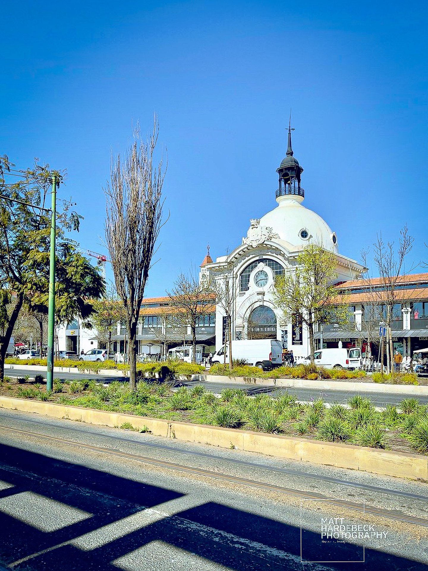White-domed facade of the Mercado da Ribeira market in Lisbon, surrounded by shops and street greenery.