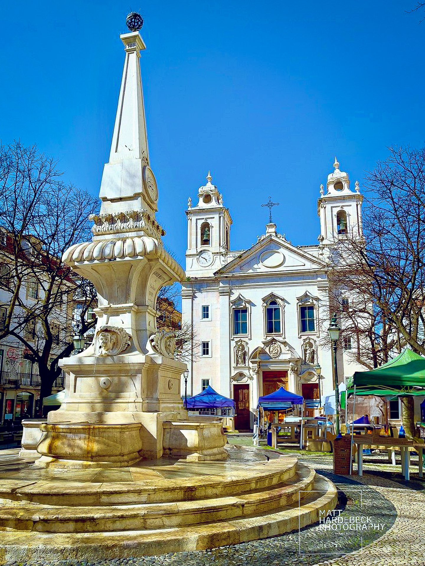 Ornate white stone fountain in Praça de São Paulo, with the church’s twin bell towers in the background.