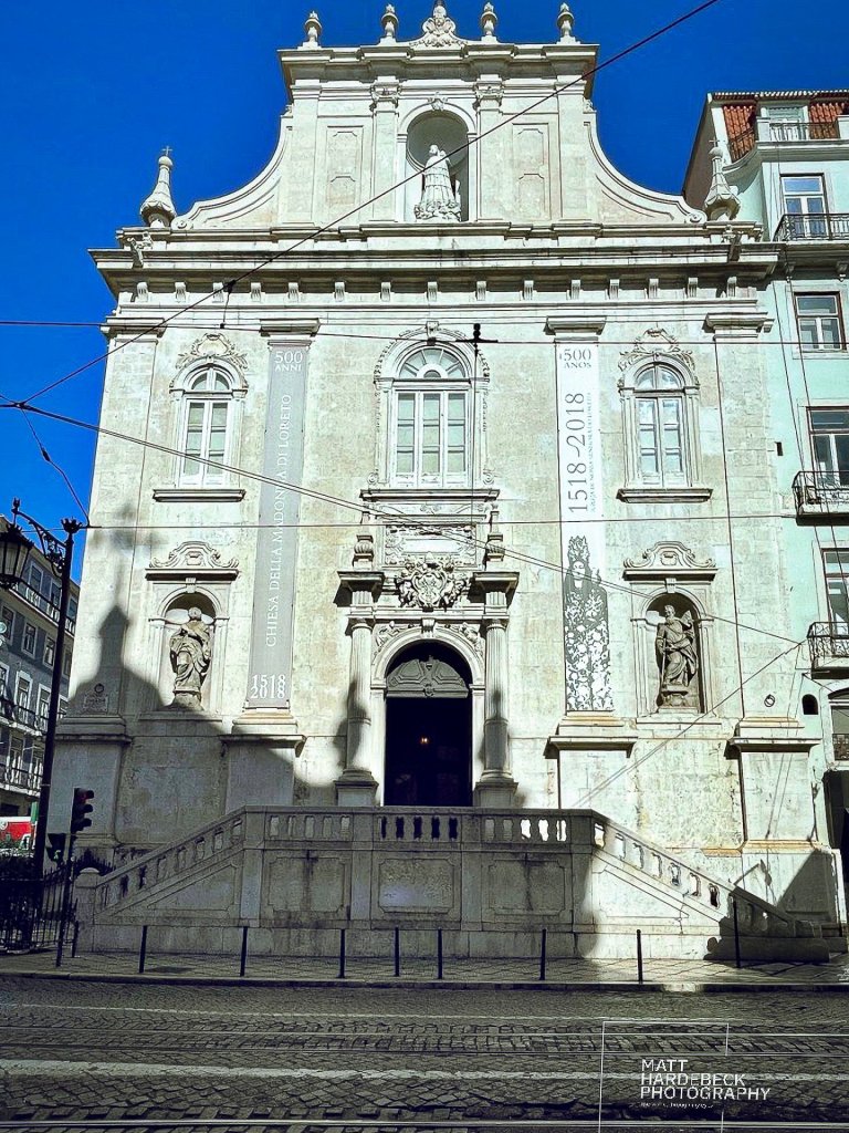 Facade of Igreja de Nossa Senhora do Loreto, a historic white stone church in Lisbon, Portugal, with statues and baroque architectural details.